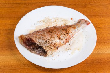 Çiğ yağda eritilmiş leş, kırmızı balık başı olmadan, aynı zamanda deniz levreği olarak da bilinir, ahşap bir masada pişirilmeden önce baharatlarla marine edilmiş.