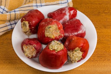Pirinçle doldurulmuş donmuş çiğ kırmızı dolma biber ve doğranmış et, son aşçılığı takip etmek için ahşap bir masada bir tabakta yatıyor.
