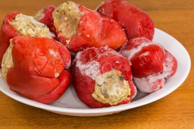 Son aşçılığı takip etmek için pirinçle doldurulmuş donmuş kırmızı dolma biber ve doğranmış et seçici bir odak noktasında, ahşap bir masada bir tabağın üzerinde uzanıyor.