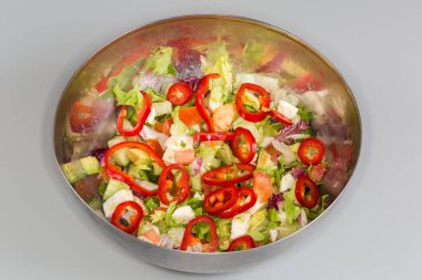 Yumuşak peynirli salata, avokado, yeşil ve kırmızı marul, dilimlenmiş tatlı biber Kapia ve diğer taze sebzeler gri arka planda paslanmaz çelik kasede.