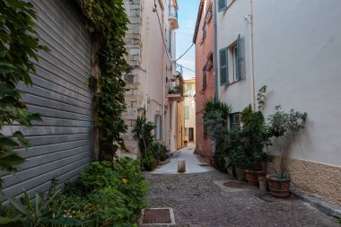 Eski kasabadaki üç katlı taş binalar arasındaki saksılarda büyüyen süs bitkileriyle süslenmiş dar bir caddenin bir parçası.