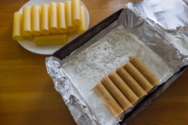Doldurulmuş büyük silindirik cannelloni makarnasının hazırlanması et dolgusu ile folyoyla kaplı bir tepside pişirmek için, üst görünüm