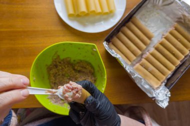 Büyük silindirik tüpler şeklinde çiğ makarna, ki buna cannelloni denir, sonraki pişirme için et dolması sırasında, üst görünüm seçici odak noktasında