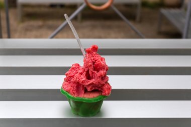 Açık bir kafedeki tek kullanımlık yeşil bardakta küçük şeffaf kaşıkla ahududulu dondurma.