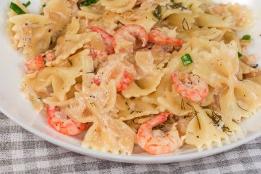 Kelebek şeklinde pişirilmiş makarna, kaynamış karides kuyruğuyla makarnaya yakın plan, masada beyaz souse.