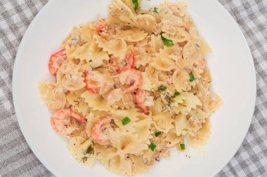 Pişmiş kelebek şekilli makarna servis ediyorum. Haşlanmış karides kuyruğu ve masa örtüsü olan bir tabakta beyaz şalgam.