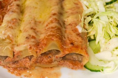 Fırınlanmış büyük silindirik makarna cannelloni peynirle doldurulmuş et, tabakta yeşil sebze salatası, yakın plan.