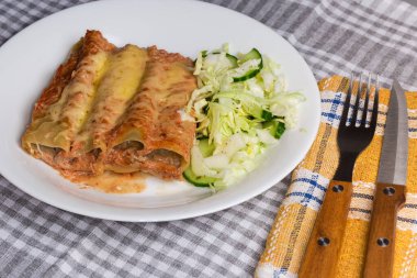 Fırınlanmış büyük silindirik makarna tüpleri, et dolgusu ile doldurulmuş, masaya yeşil sebze salatası serpiştirilmiş, yakın çekim