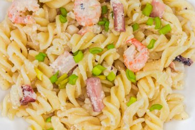 Pişmiş spiral makarna, haşlanmış karides kuyruğu ve diğer deniz ürünleri ile birlikte yakın plan beyaz bir tabakta.