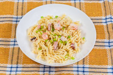 Haşlanmış karides kuyruğu ve diğer deniz mahsulleri ile Rotini olarak adlandırılan pişmiş spiral makarna servis ediliyor. Masada kareli masa örtüsüyle kaplı bir tabakta.