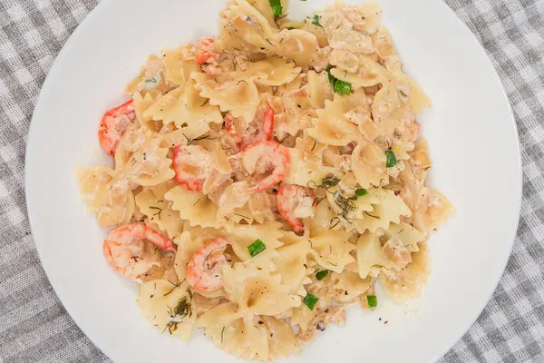 Pişmiş kelebek şekilli makarna servis ediyorum. Haşlanmış karides kuyruğu ve masa örtüsü olan bir tabakta beyaz şalgam.