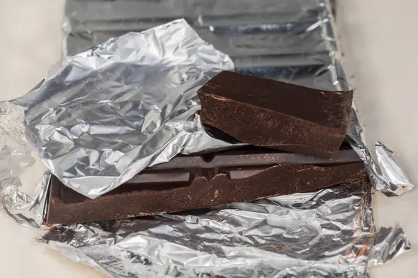 Çikolatadan kopmuş bir parça siyah çikolata. Açık kâğıt ambalajında biraz yırtık folyo ambalajı. Seçici odak noktasında yakın plan görüntü.