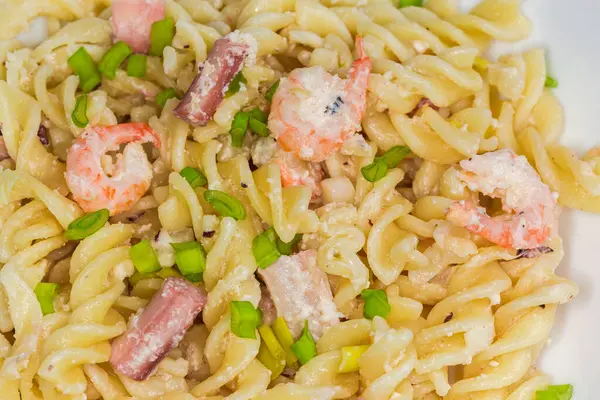 Pişmiş spiral makarna, haşlanmış karides kuyruğu ve diğer deniz ürünleri ile birlikte yakın plan beyaz bir tabakta.