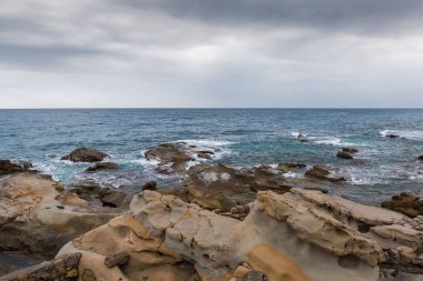 Kıyı şeridi ile su yüzeyinin bir kısmı arasındaki deniz dalgaları sonbaharda bulutlu bulutlu hava koşullarında sörf yapıyor.