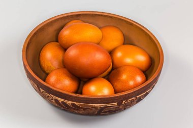 Birkaç Paskalya yumurtası gri arka planda bitki desenleriyle süslenmiş kilden bir kasede kahverengiye boyanmış.