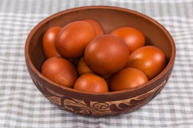 Kareli masa örtüsüyle kaplı bir masanın üzerindeki bitki deseniyle süslenmiş kilden bir kasede kahverengi boyanmış birkaç Paskalya yumurtası.