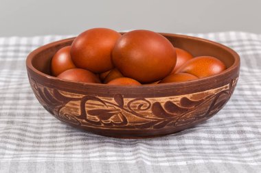 Birkaç Paskalya yumurtası kil bir kaseye boyanmış. Kareli masa örtüsüyle kaplı bir masada bitki deseniyle süslenmiş. Önden seçici bir odak noktasında.