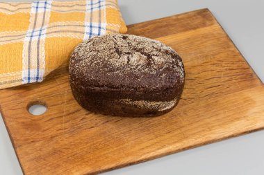 Küçük bir somun çavdar ekmeği ile buğday esmer ekmek Eski bir ahşap kesme tahtasına dökülen irmik serpiştirilmiş gri yüzey üzerindeki kumaş peçetesine karşı