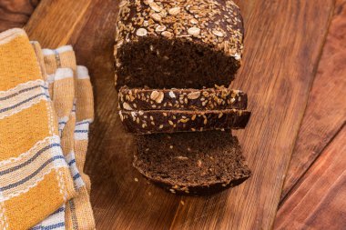 Kısmen dilimlenmiş çavdar ekmeği, susam ve keten tohumlarıyla süslenmiş, ahşap bir kesme tahtasında, masa, üst manzara