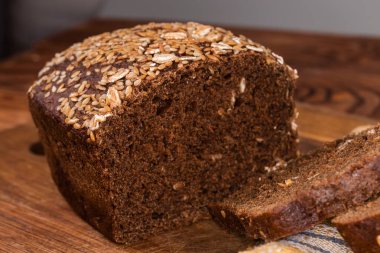 Kısmen dilimlenmiş çavdar-buğday ekmeği, susam ve keten tohumları ile süslenmiş, tahta kesme tahtasındaki taneler, seçici odak noktasında yakın plan