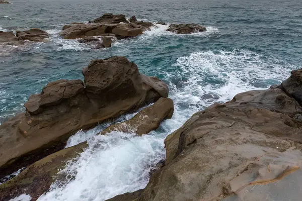 Sonbaharda yağmurlu havalarda, taştan bir sahil şeridinin kıyı kayaları ve su yüzeyinin bir kısmı arasında sörf dalgaları.