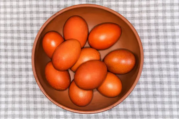 Birkaç Paskalya yumurtası kil bir kâsede kareli masa örtüsüyle kaplanmış bir masada kahverengi renge boyanmış.