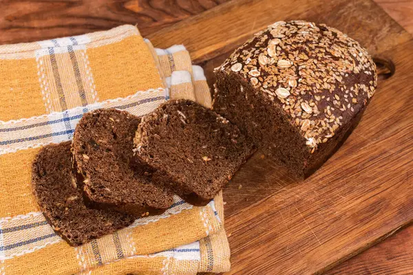Kısmen dilimlenmiş çavdar ekmeği, susam ve keten tohumlarıyla süslenmiş, ahşap bir kesme tahtasındaki peçeteyle, masa, üst manzara