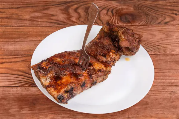 Baharatla pişirilmiş domuz pirzolası ve özel souse ile doldurulmuş domuz pirzolası kırsal bir masada büyük beyaz bir tabağa saplanmış.