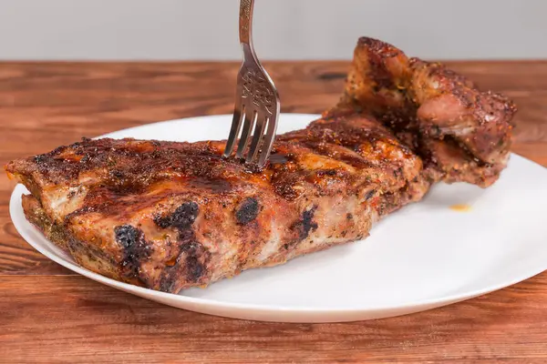 Baharatla pişirilmiş ve özel souse ile doldurulmuş domuz kaburgalarının tamamı, büyük beyaz bir tabağın çatalına saplanmış, kırsal bir masada, ön manzara seçici odak noktasında.