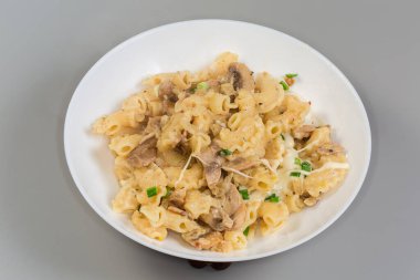 Taze pişirilmiş kısa kıvrımlı makarna servisi, Creste di gallo, ya da gri arka plandaki bir tabakta mantar ve peynirli horoz tarağı.