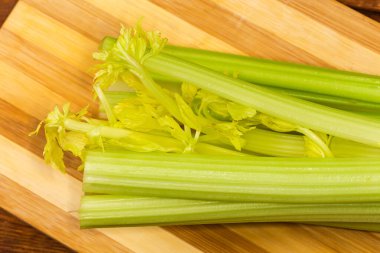 Taze kereviz sapları, ahşap kesme tahtasının üzerinde kırpılmış yapraklar, yakın çekim parçasının üst görüntüsü.