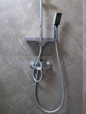 Karıştırıcı musluğu ve çıkarılabilir dikdörtgen duş başlığını paranteze yerleştirilmiş esnek hortumla gri fayanslı duvara karşı iç duşta tut