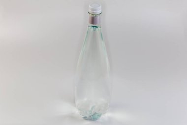 Gri arka planda kapalı vida kapaklı plastik şeffaf maden suyu şişesi.