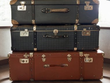 Stack of the closed old big rectangular-shaped old-fashioned shabby hardshell suitcases, made with leatherette of different color
