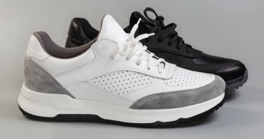 Biri siyah, diğeri beyaz, klasik tarzda bir spor ayakkabı. Gri bir arka planı var, seçici odak noktasında yan görünümü var.