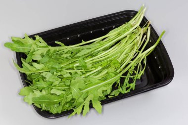 Gri arka plandaki siyah plastik kapta toplanan taze roka kökleri.