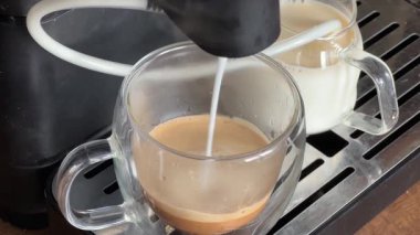 Kahve makineli kahve bardağına kaşlarını çatarak süt dökmek.