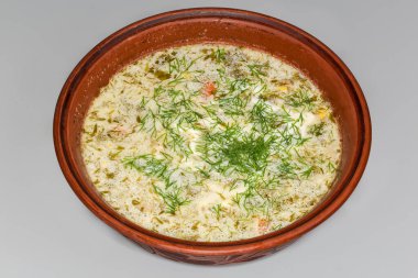 Yeşil borş olarak da bilinen kuş çorbasının bir kısmı ekşi krema ve gri bir zemin üzerinde killi bir kasede taze doğranmış dereotu serpiştirilmiş.