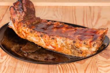 Özel sosta pişirilmiş domuz kaburgalarının tamamı büyük siyah bir tabakta, ahşap bir kırsal masada, yakın çekimde seçici bir odak noktasında.