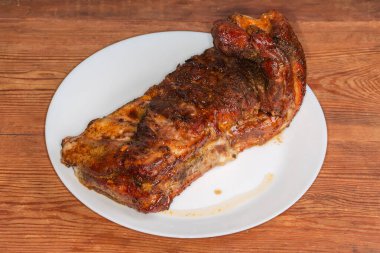 Özel sosla pişirilmiş domuz kaburgalarının tamamı ahşap bir kırsal masada büyük beyaz bir tabakta yatıyor.