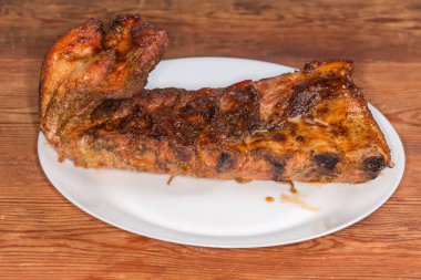 Özel sosta pişirilmiş domuz kaburgalarının tamamı büyük beyaz bir tabakta, ahşap bir kırsal masada, seçici bir odak noktasında yan görüşte.