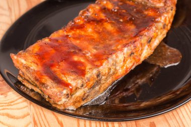 Özel sosta pişirilmiş domuz kaburgalarının tamamı masanın üzerindeki büyük siyah bir tabakta duruyor.