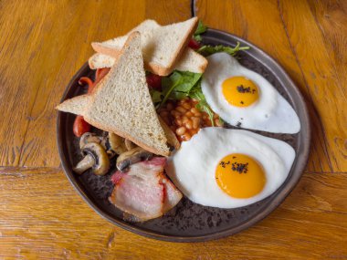 İki kızarmış yumurtalı kahvaltı. Mantar, domuz pastırması, ince sosis, kaynamış fasulye ve ekmek dilimleri ile servis edilmiş. Eski bir meşe ağacının üstünde.