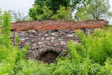 Eski savunma duvarının bir parçası. İlkbahar bulutlu günlerinde yıkılmış ortaçağ şatosunda ağaçlar ve çalılarla kaplanmış taştan ve kırmızı tuğladan yapılmış.