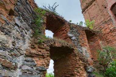 Eski savunma duvarının bir parçası ve taş ve kırmızı tuğladan yapılmış kule. İlkbahar bulutlu bir günde yıkılmış ortaçağ kalesinde çimlerle ve genç ağaçlarla kaplanmış. Seçici bir odak noktasında.