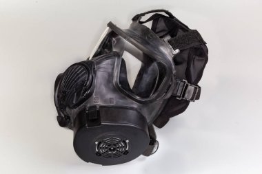 Siyah kauçuk gaz maskesi, maskenin yanına takılı gri arka plan, yan görüş.