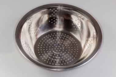 Boş yuvarlak kase şeklinde paslanmaz çelik kevgir sapları olmadan gri arka planda uygun bir mutfak kasesine yerleştirilir.