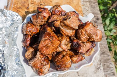 Mangal kömürü üzerine ızgara yapılmış Shashlik parçaları yığını ve açık havada büyük beyaz mutfak kasesindeki şişler kaldırıldı.