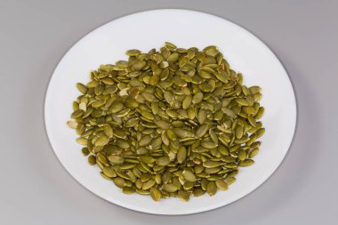 Kuru kabak çekirdekleri kabuklarından soyulmuş gri bir zemin üzerindeki beyaz tabakta.