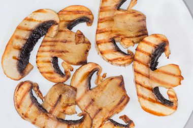 Beyaz bir tabakta büyük düğmeli mantarın ince ızgara dilimleri, parçanın üst görüntüsü.